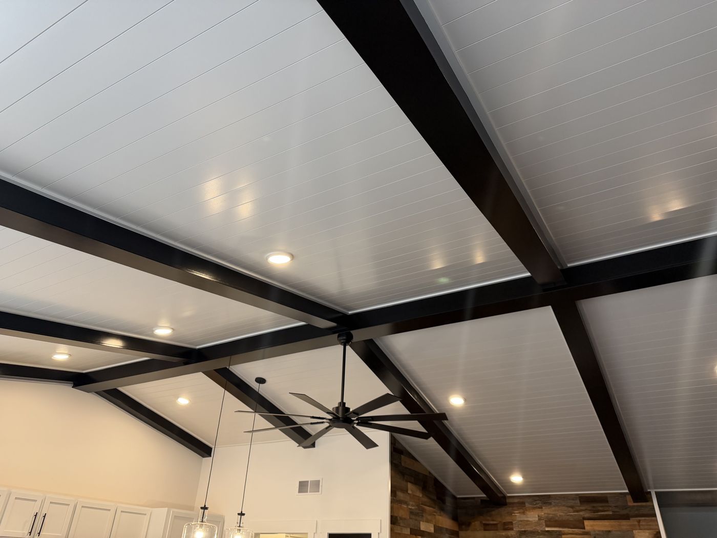 Black beam grid on a white plank ceiling with fan and recessed lights