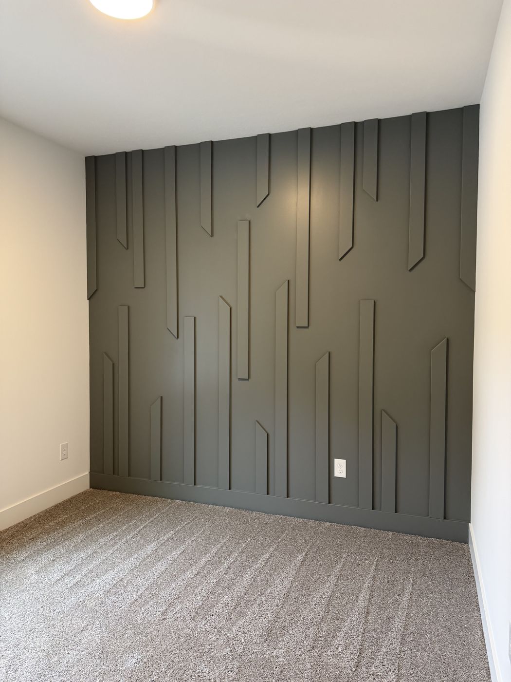 After: Finished charcoal geometric batten accent wall in a carpeted bedroom