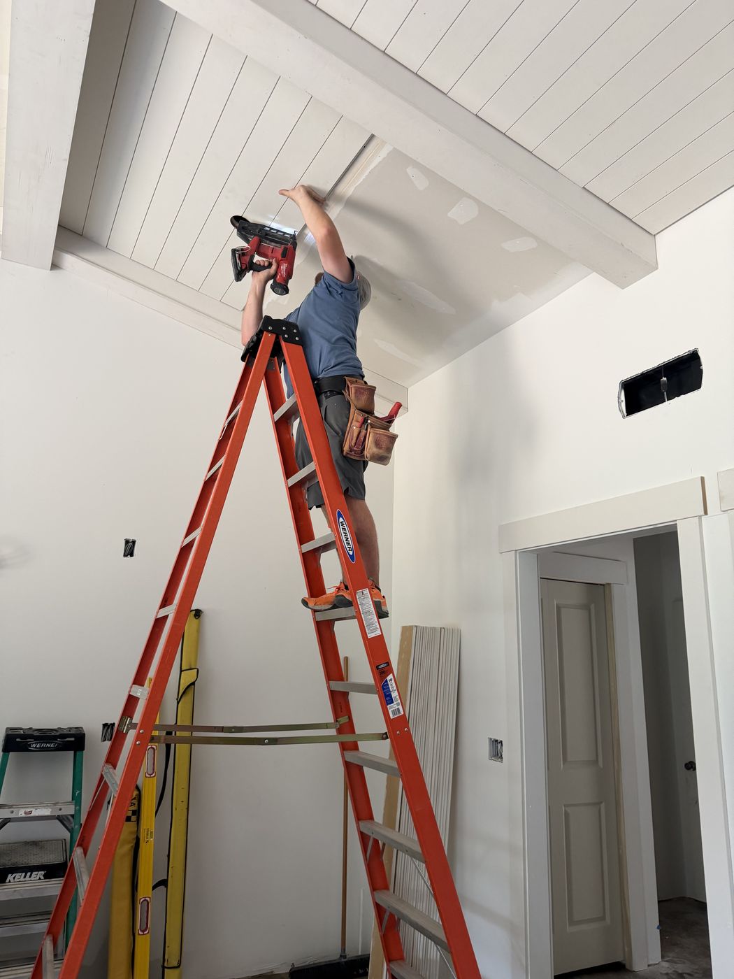 Carpenter on a ladder installing white ceiling planks