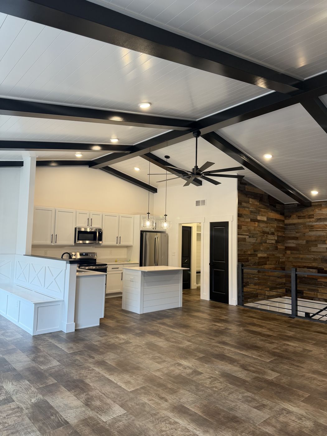 Finished great room with black beamed ceiling, white kitchen, banquette, and stair rail