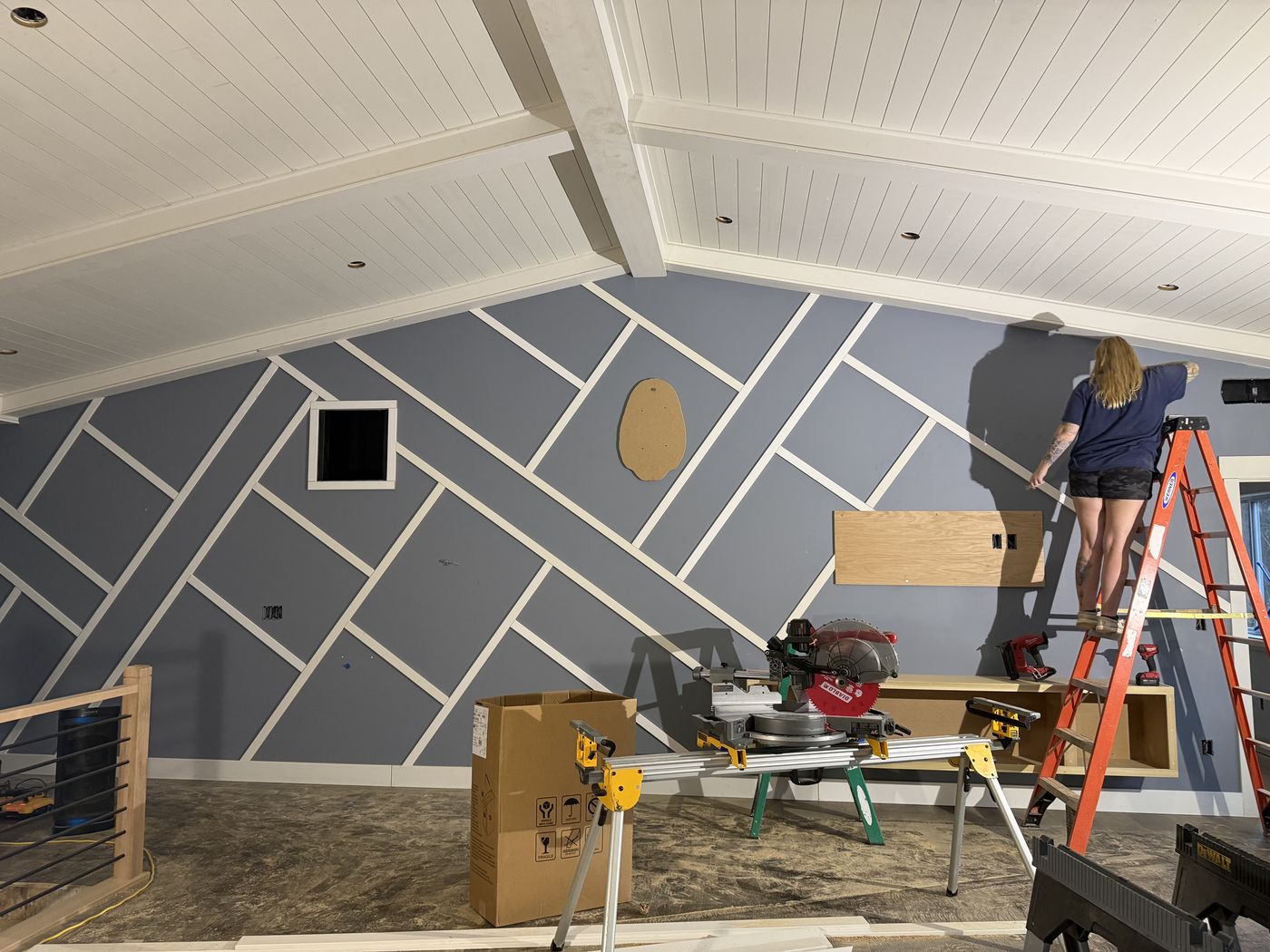 Before: Nicole on a ladder installing diagonal battens on the great room wall