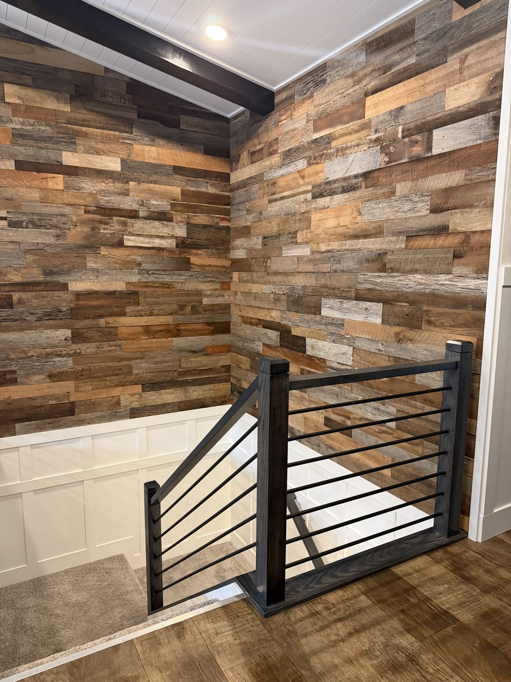 After: Finished dark stair rail with horizontal bars in front of a weathered wood plank wall