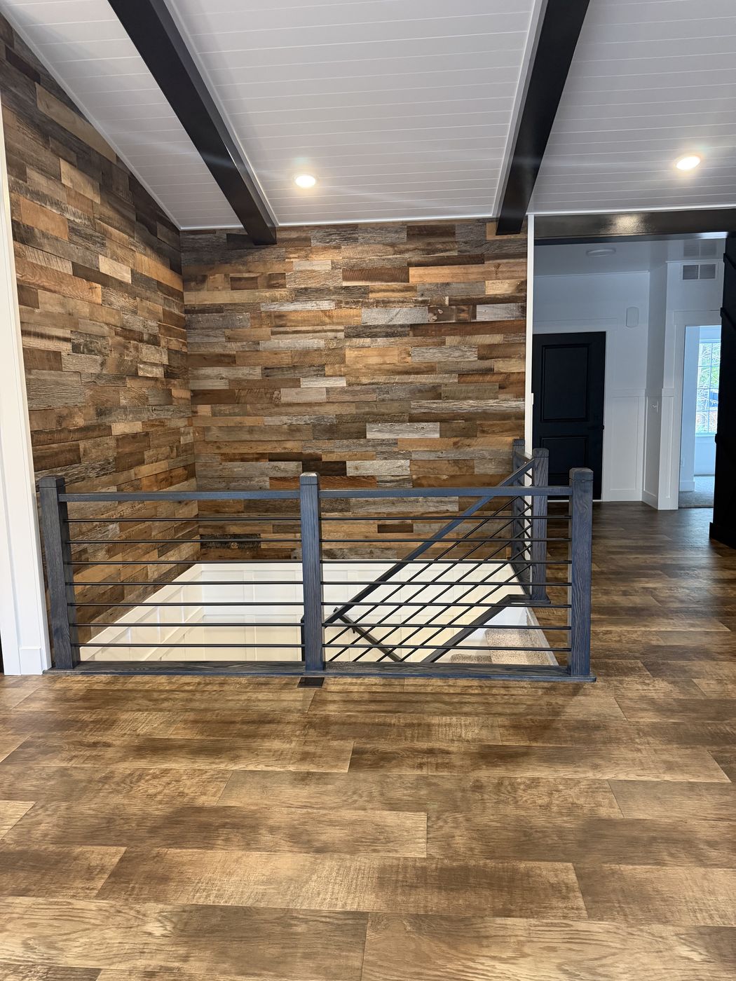 Stair landing with dark horizontal-bar rail and weathered wood plank wall